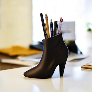 May include: A black high-heeled boot shaped desk organiser with pens and pencils inside.