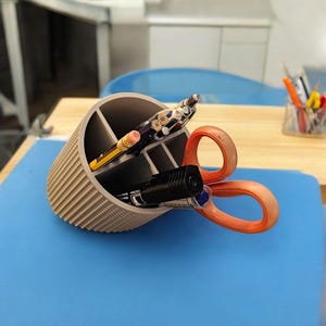 May include: A beige desk organiser with four compartments holds a black marker, a yellow pencil, a multi-coloured pen, and a pair of orange scissors.