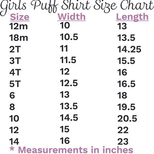 Op de afbeelding: Maattabel voor meisjes puff shirts van AJ Blanks, met maten van 12 maanden tot 14. De tabel geeft breedte- en lengtematen in inches, vari&euml;rend van 25,4 cm breed tot 58,4 cm lang.