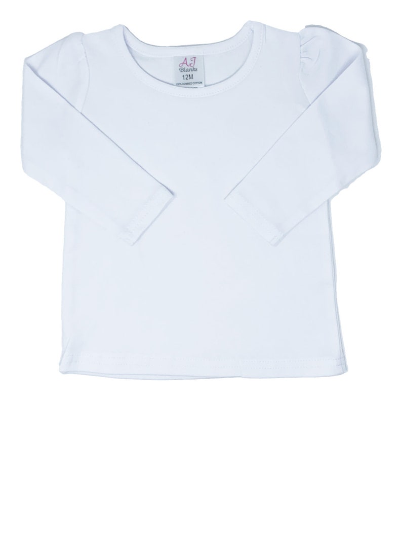 May include: A white long-sleeved shirt with a round neckline and a small tag near the collar. The tag reads "AJ Blanks 12M". The shirt has a simple, classic design, suitable for various occasions. The sleeves have a slight puff detail at the shoulders.