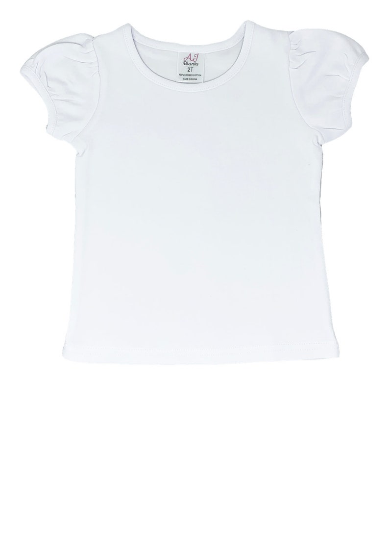 May include: A white short-sleeved t-shirt with a round neckline and puffed sleeves. The tag reads "A.J. Blanks 2T". The shirt is made of 100% cotton and is made in China. This shirt is perfect for children.