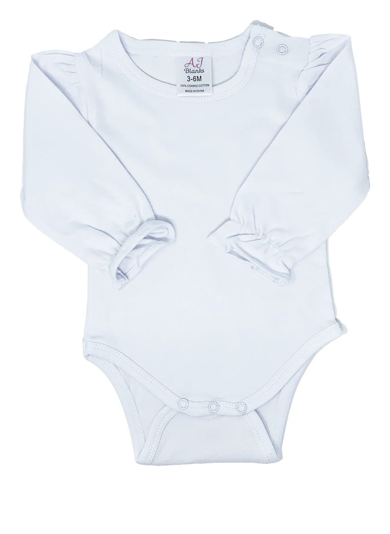 May include: White long-sleeved baby bodysuit with a round neckline and snap closures. The bodysuit has ruffled sleeves and shoulders. The label reads "AJ Blanks 3-6M 100% combed cotton Made in China."