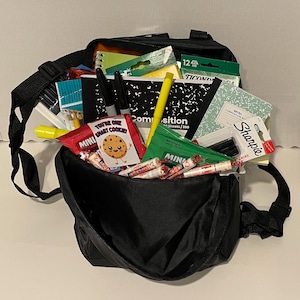 May include: A black backpack filled with school supplies and snacks. Contents include notebooks, pens, highlighters, and candy. A small package reads "You're One Smart Cookie!"