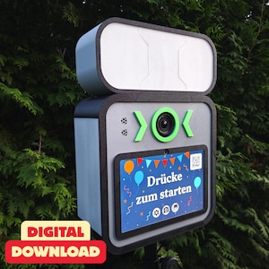 Könnte beinhalten: Eine grau-schwarze Fotobox mit hellblauer Seitenwand und weißer Oberseite. Die Box hat eine Kamera mit grünen Akzenten und einen Bildschirm mit dem Text "Drücke zum starten" mit bunten Luftballons und einem QR-Code.