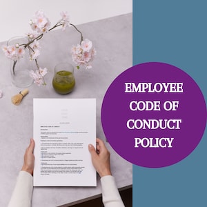 Peut inclure: Une feuille de papier blanche avec le texte "Employee Code of Conduct" en haut. Le papier est tenu par les mains d'une personne. L'arrière-plan est une surface gris clair avec un verre de thé vert et un vase de fleurs roses.