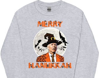 May include: A grey long-sleeved t-shirt featuring a graphic of a person wearing a witch's hat and a suit with a bat pattern. The text "Merry Hanukkah" is printed on the shirt.