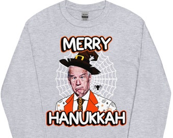 May include: A grey long-sleeved t-shirt featuring the text "Merry Hanukkah" and a cartoon image of a person wearing a witch's hat and a costume with a spider web behind them.