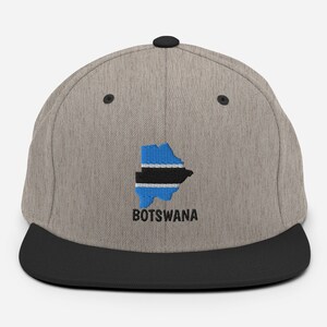 May include: A gray and black flat brimmed baseball cap with an embroidered outline of Botswana and the word "BOTSWANA" in black.
