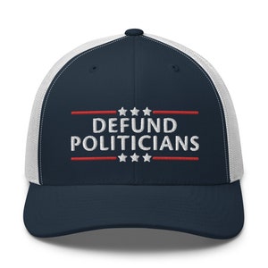 May include: Navy blue and white trucker hat with the text "DEFUND POLITICIANS" embroidered in white, with red lines and stars. The hat has a mesh back and a curved brim.