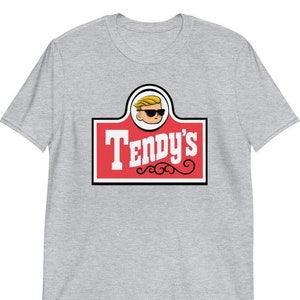 May include: A gray t-shirt with a red and white logo that says "Tendy's". The logo features a cartoon character with blonde hair and sunglasses.