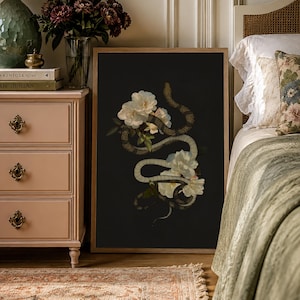 May include: A framed rectangular wall art print featuring a dark black background with a detailed illustration of a winding snake intertwined with several large, pale white peony flowers. The artwork is encased in a simple, light-toned wooden frame.