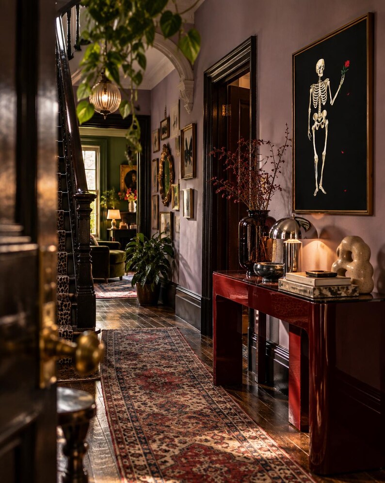 May include: A hallway interior featuring a glossy dark red console table, a framed black wall art piece depicting a skeleton holding a red rose, a patterned runner rug, a dark staircase with leopard print carpet, and various decorative home accents.