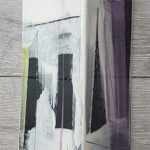 May include: A white ceramic vase with abstract black, gray, and purple brushstrokes. The vase has a rectangular shape with a slightly angled top.