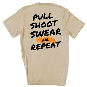 Puede incluir: Camiseta de color beige con texto negro que dice "Pull Shoot Swear and Repeat" con dos platos de arcilla naranja.