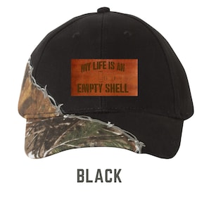 May include: Black baseball cap with a camouflage brim and a brown leather patch that says "My life is an empty shell" with a bullet casing graphic.