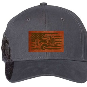 Op de afbeelding: Een donkergrijze baseballpet met een bruine leren patch met een Amerikaanse vlag en een silhouet van een vrachtwagen.
