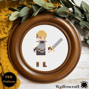 May include: A cross-stitch pattern of a pixelated character holding a sword. The character has blonde hair, a gray tunic, and brown boots. The pattern is framed in a brown wooden frame.
