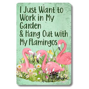 May include: A metal sign with a green background and white text that reads "I Just Want to Work in My Garden & Hang Out with My Flamingos". The sign features a watercolor illustration of three pink flamingos in a garden setting with flowers and greenery.