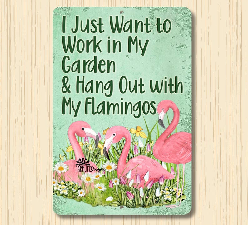 May include: Metal sign with a green background and white text that reads "I Just Want to Work in My Garden & Hang Out with My Flamingos". The sign features a watercolor illustration of three pink flamingos in a garden setting with yellow flowers and green grass.
