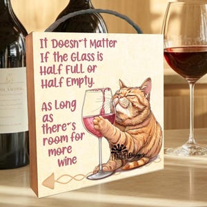 May include: A wooden sign with a cat drinking wine. The sign reads "It Doesn't Matter If the Glass is Half Full or Half Empty. As Long as there's room for more wine."
