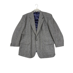 May include: A gray tweed blazer with a navy blue lining, hanging on a clear hanger. The blazer has two front pockets and a single button closure. The fabric has a subtle herringbone pattern.