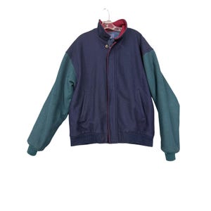 May include: A navy blue jacket with teal sleeves and a red collar. The jacket has a button closure and two front pockets. The jacket is hanging on a hanger against a white background.