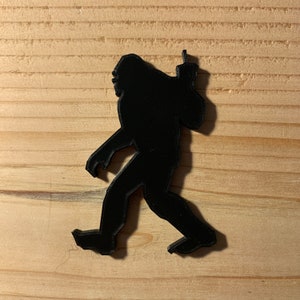 Könnte beinhalten: Schwarze Silhouette eines Bigfoots mit einem erhobenen Arm in einem Mittelfinger-Gestus.