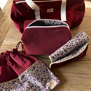 Könnte beinhalten: Set aus vier burgunderfarbenen Cordtaschen mit weißen Griffen und Blumenfutter. Die größte Tasche ist eine Reisetasche, die nächste ist eine Kosmetiktasche und die beiden kleinsten sind Beutel mit Kordelzug.