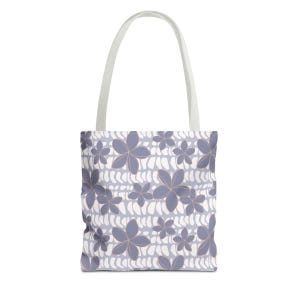 May include: A tote bag featuring a repeating pattern of purple five-petaled flowers with thin gold outlines. The background consists of horizontal rows of white, rounded, pill-shaped marks on a light purple field. It has two white fabric handles.