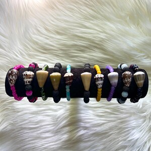 May include: A collection of beaded bracelets with various designs. Each bracelet features a unique combination of beads, including lava rock, colorful beads, and cone-shaped shells. The bracelets are displayed on a black velvet surface.