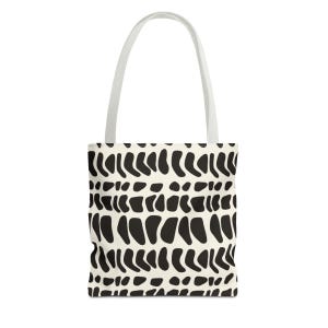 May include: A cream-colored tote bag featuring a repeating pattern of black, irregular, rounded shapes arranged in horizontal rows. The bag has two long, white fabric handles attached to the top, providing a simple and functional design.