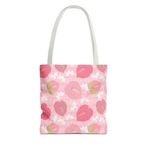 May include: A tote bag featuring a repeating pattern of pink anthurium flowers and small white blossoms on a light pink background. The bag has two white shoulder straps attached to the top, providing a simple and functional design for carrying items.
