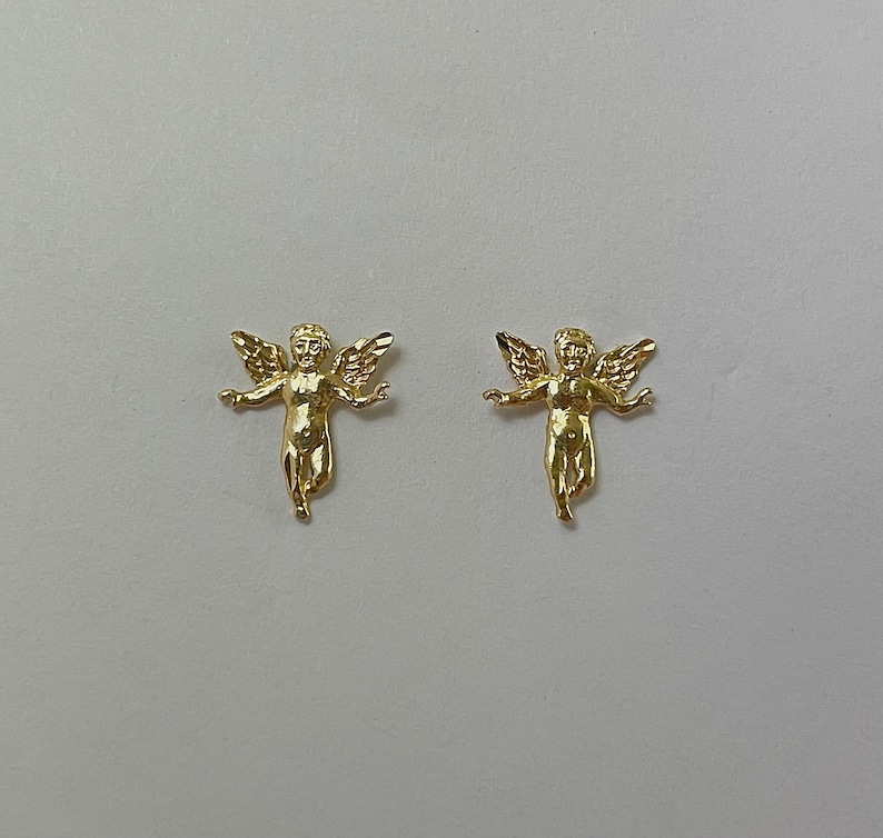 Pu&ograve; includere: Due statuette dorate di cherubini con le braccia tese e ali dettagliate. I cherubini sono rivolti in avanti, con una finitura liscia e lucida. Lo sfondo &egrave; di colore grigio chiaro uniforme. Queste statuette sono probabilmente oggetti decorativi.