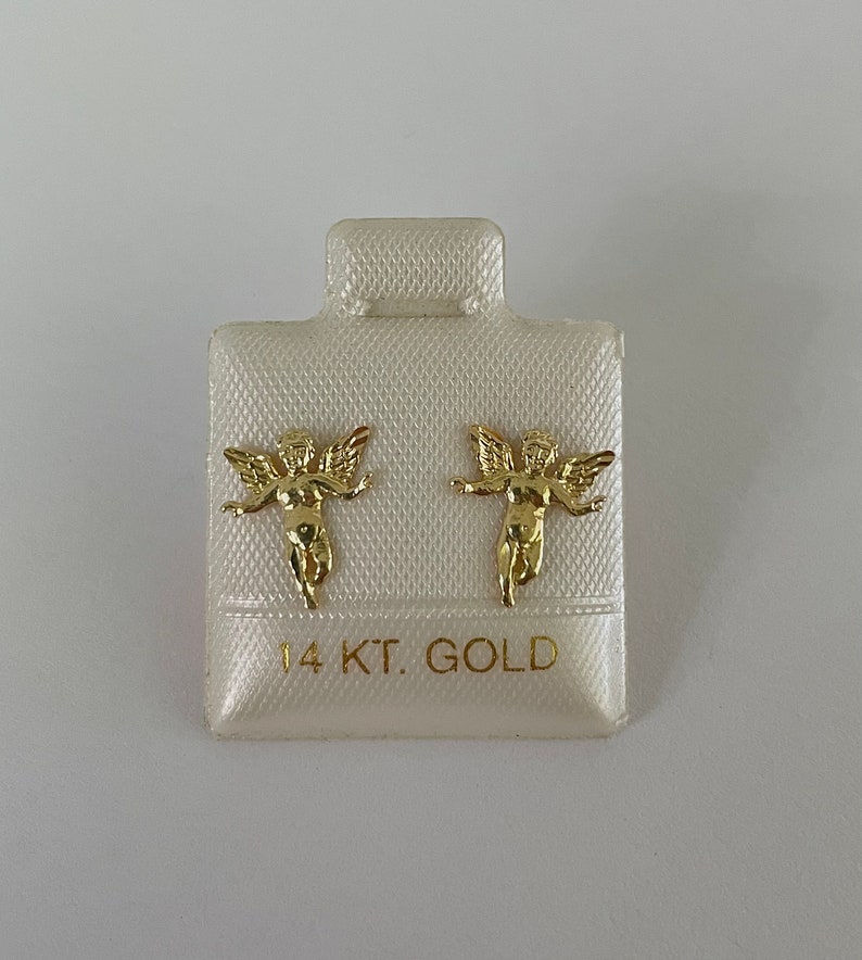 Pu&ograve; includere: Un paio di orecchini a lobo a forma di angelo color oro su un cartoncino bianco. Gli orecchini presentano un design dettagliato di cherubino con ali spiegate. Il cartoncino &egrave; etichettato "14 KT. GOLD".