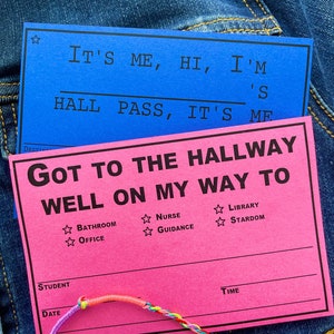 Könnte beinhalten: Zwei farbenfrohe Schülerausweise auf Denim. Der blaue Ausweis lautet "It's me, hi, I'm hall pass, it's me." Der rosa Ausweis lautet "Got to the hallway well on my way to" mit Optionen wie Badezimmer und Büro. Ein Regenbogen-Freundschaftsarmband ist im Vordergrund.
