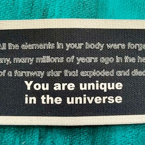 May include: A rectangular black and white sign with the text "All the elements in your body were forged many, many millions of years ago in the heart of a faraway star that exploded and died. You are unique in the universe."