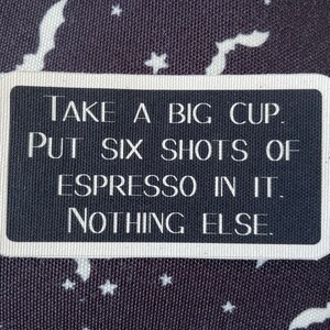 May include: A rectangular black and white sign with rounded corners. The sign reads "TAKE A BIG CUP. PUT SIX SHOTS OF ESPRESSO IN IT. NOTHING ELSE." The background is a dark fabric with white bats and stars.
