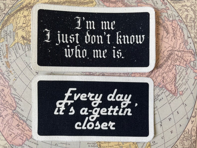 May include: Two rectangular patches with black backgrounds and white text. The top patch reads "I'm me, I just don't know who me is." The bottom patch says "Every day, it's a-gettin' closer."