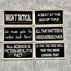 Könnte beinhalten: Sechs schwarze rechteckige Schilder mit weißem Text auf gemustertem Hintergrund. Die Schilder zeigen Sätze wie "WASN'T TACTICAL" und "A SEAT AT THE END OF TIME". Die Schilder haben weiße Ränder.