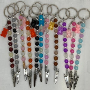 May include: A selection of beaded keychains with silver metal clips. Each keychain has a different colour scheme of beads and a small gummy bear charm. The keychains are attached to silver key rings.