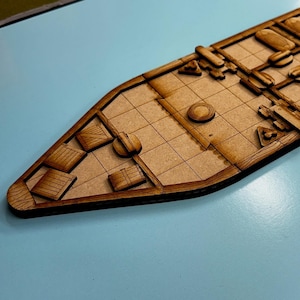 May include: A wooden model ship deck with a grid pattern and several small wooden boxes. The deck is brown and has a light brown stain.