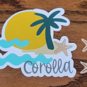 May include: A die-cut sticker featuring a beach scene with a yellow sun, palm tree, and ocean waves. The word "Corolla" is written in a script font. Three starfish are also included.