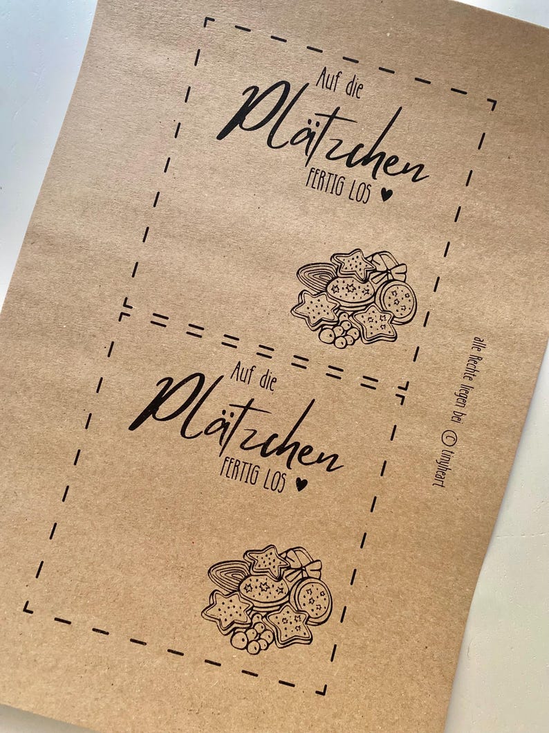 May include: Brown paper with two printed sections featuring the text "Auf die Pl&auml;tzchen FERTIG LOS" and a heart symbol. Each section includes a drawing of various cookies.