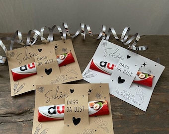 May include: Three gift cards with a Kinder chocolate bar attached. The cards have the text "Schön dass du da bist" and "2026 Komm gut rein" printed on them, along with decorative hearts and fireworks.