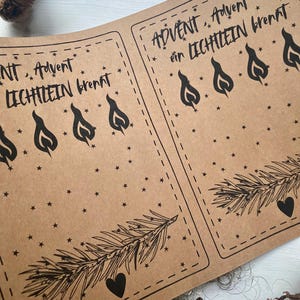 May include: Kraft paper sheets with the text "Advent, Advent ein Lichtlein brennt" in black script. The design includes black flame illustrations, stars, a sprig of pine, and a heart. The sheets are for a holiday theme.
