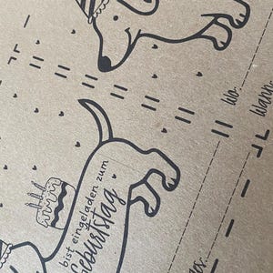 Puede incluir: Tarjeta marr&oacute;n con dibujos lineales negros de perros salchicha con gorros de fiesta y pasteles de cumplea&ntilde;os. El texto "bist eingeladen zum Geburtstag" est&aacute; escrito en una fuente de escritura.