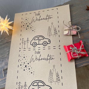 May include: Kraft paper Christmas gift tags with black line art of cars, trees, and stars. The words "Frohe Weihnachten" are written in script. Two small wrapped gifts are on the right.