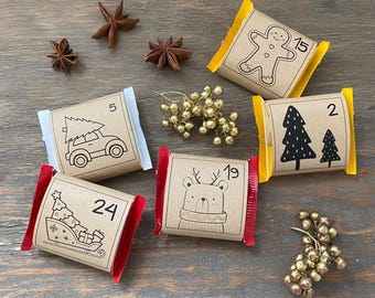 May include: An assortment of wrapped Christmas advent calendar treats. Each package is brown with a different black and white holiday illustration and a number. Some packages have red or yellow edges. Star anise and gold berries are scattered around.