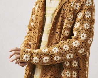 Puede incluir: Una chaqueta de punto de ganchillo marrón con flores blancas en forma de margarita. La chaqueta tiene cuello y cierre de botones.
