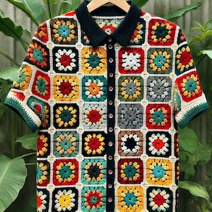 May include: A colorful crocheted shirt with a button-up front and short sleeves. The shirt is made of a variety of colors, including red, yellow, green, and blue. The shirt is hanging on a wooden hanger.